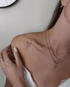 a woman with a heart tattoo on her left shoulder, next to a wall clock