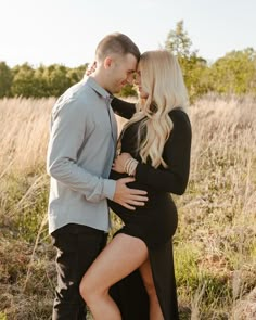 a pregnant couple cuddles in a field with tall grass