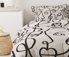 a bed with black and white designs on the comforter next to a wicker basket