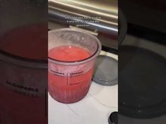 a cup filled with red liquid sitting on top of a counter next to a blender