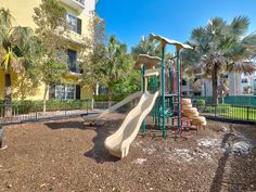 a playground with slides and palm trees in front of a multi - story apartment building