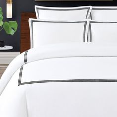 a bed with white sheets and black trimmings in a hotel room next to a potted plant