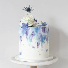 a white cake with blue and purple icing on a wooden stand next to a wall