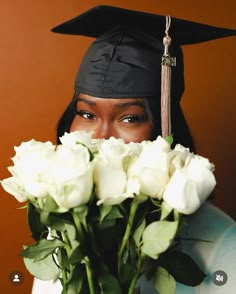 a woman wearing a graduation cap and gown holding white roses in front of her face