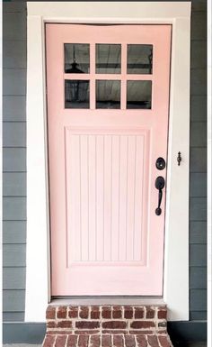 a pink front door with brick steps and white trim on the side of a house