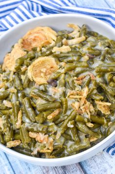 a white bowl filled with green beans covered in gravy next to a blue and white towel