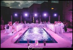 a group of people sitting around a pool at night