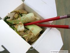 two red chopsticks in a white box filled with food