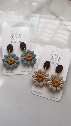 two pairs of flower earrings sitting on top of a white table next to each other