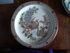 a plate with two peacocks painted on it sitting on a table next to a bowl