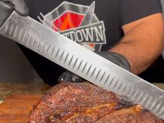 a man holding a large knife over a piece of meat on top of a cutting board