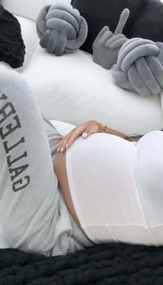 a woman laying on top of a white bed next to two gray stuffed animals in the shape of hands