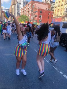 two women in colorful skirts are dancing on the street while people walk by behind them