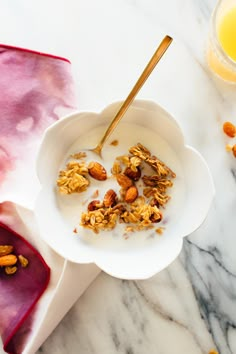 a white bowl filled with granola next to a glass of orange juice on a marble table