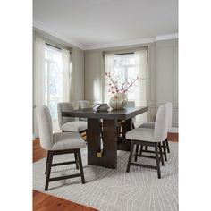 a dining room table with four chairs and a vase on top of it in front of windows