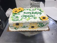 a birthday cake with sunflowers on it sitting on top of a metal table