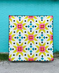 a colorful quilt hanging on the side of a blue brick wall in front of a building