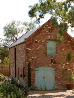 an old brick building with green shutters and blue doors is surrounded by greenery