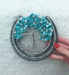 a woman's hand holding a small tree brooch with turquoise beads on it