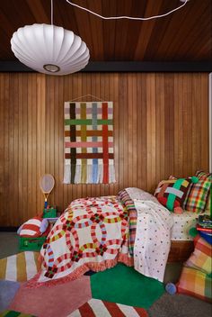 a bedroom with wood paneling and colorful bedspreads on the floor, lights hanging from the ceiling