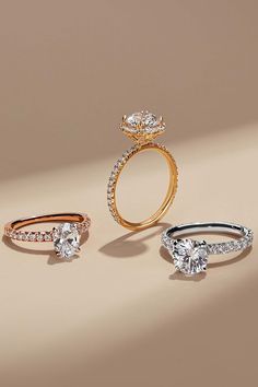 three different types of engagement rings on a beige background, one with an oval diamond and the other with round brilliant cut diamonds