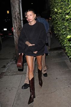 a woman in black sweater and shorts walking down the street with her hand on her hip