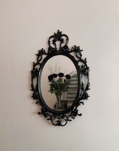 a mirror hanging on the wall above a vase with flowers in it and a plant