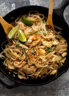 a plastic container filled with noodles and veggies next to a lime wedge on the side