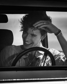 a woman sitting in the driver's seat of a car with her hand on her head