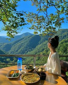 a woman sitting at a table with plates of food in front of her, overlooking the mountains