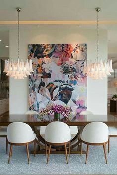 a dining room table with white chairs and a large painting on the wall behind it