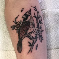 a small bird sitting on top of a tree branch with leaves and flowers around it