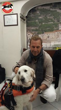 a man sitting in front of a white dog wearing an orange life jacket and black scarf