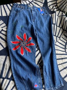 a pair of blue jeans with red flowers on them sitting on top of a patterned cloth