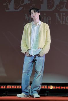 a man standing on top of a stage in front of a projector screen with his hands in his pockets