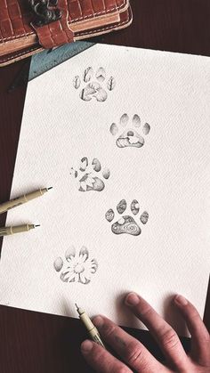 a person is holding a pen and drawing paw prints on paper with watercolor pencils