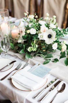 the table is set with white flowers and silverware