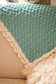 a green crocheted blanket sitting on top of a couch next to a pillow