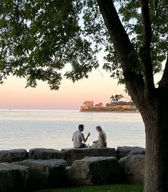 two people sitting on rocks near the water