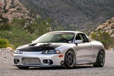 a silver sports car parked on the side of a road in front of some mountains