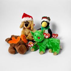 three stuffed animals are sitting next to each other on a white surface, one is wearing a santa hat