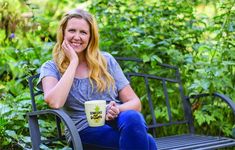 a woman sitting on a bench with a coffee cup in her hand and smiling at the camera