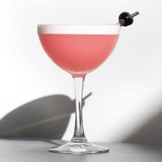 a pink drink in a wine glass with a black olive garnish