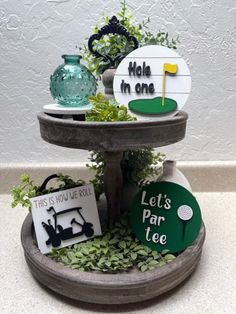 two tiered trays with golf signs and plants on them, one holding a hole in one sign that says let's fair tee