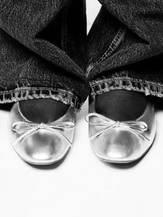 black and white photograph of someone's feet wearing silver shoes with bows on them