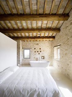 a bedroom with a bed and a bathtub in it's center, surrounded by stone walls