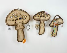 three mushrooms are hanging on the wall with beaded earring hooks in front of them