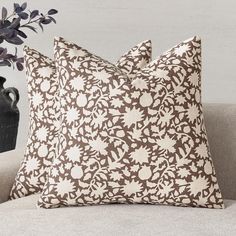 two brown and white pillows sitting on top of a couch next to a vase with purple flowers