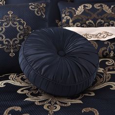 a black round pillow sitting on top of a bed next to blue pillows and blankets