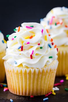 three cupcakes with white frosting and sprinkles on a table